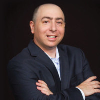 Steven_Mostyn seen in suit with his hands folded and posing for a photo